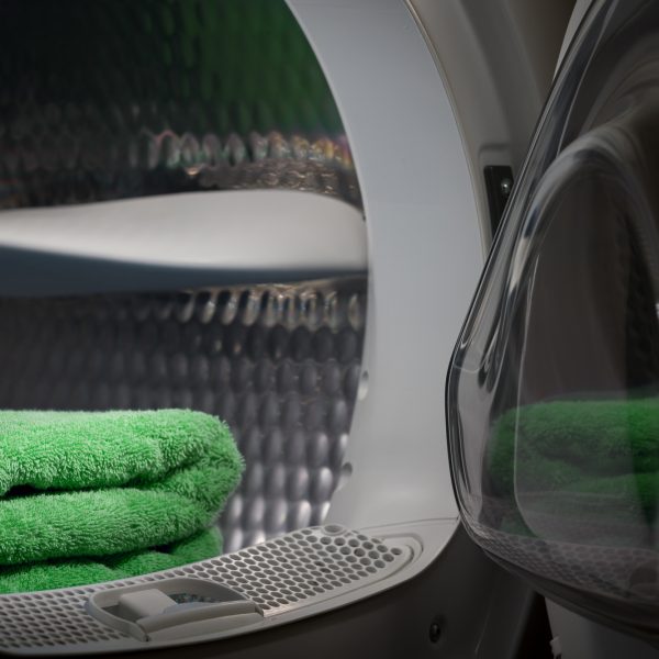 dryer-with-open-door-in-a-dark-room-with-green-towels-are-stacked-inside-the-drum